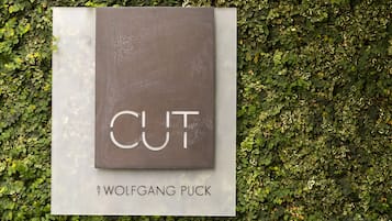 A sign with the word "CUT" and the text "by Wolfgang Puck" against a backdrop of a green leafy wall.