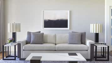 A modern living room with a light-colored sofa, two side tables with lamps, a framed abstract painting, and a marble coffee table.