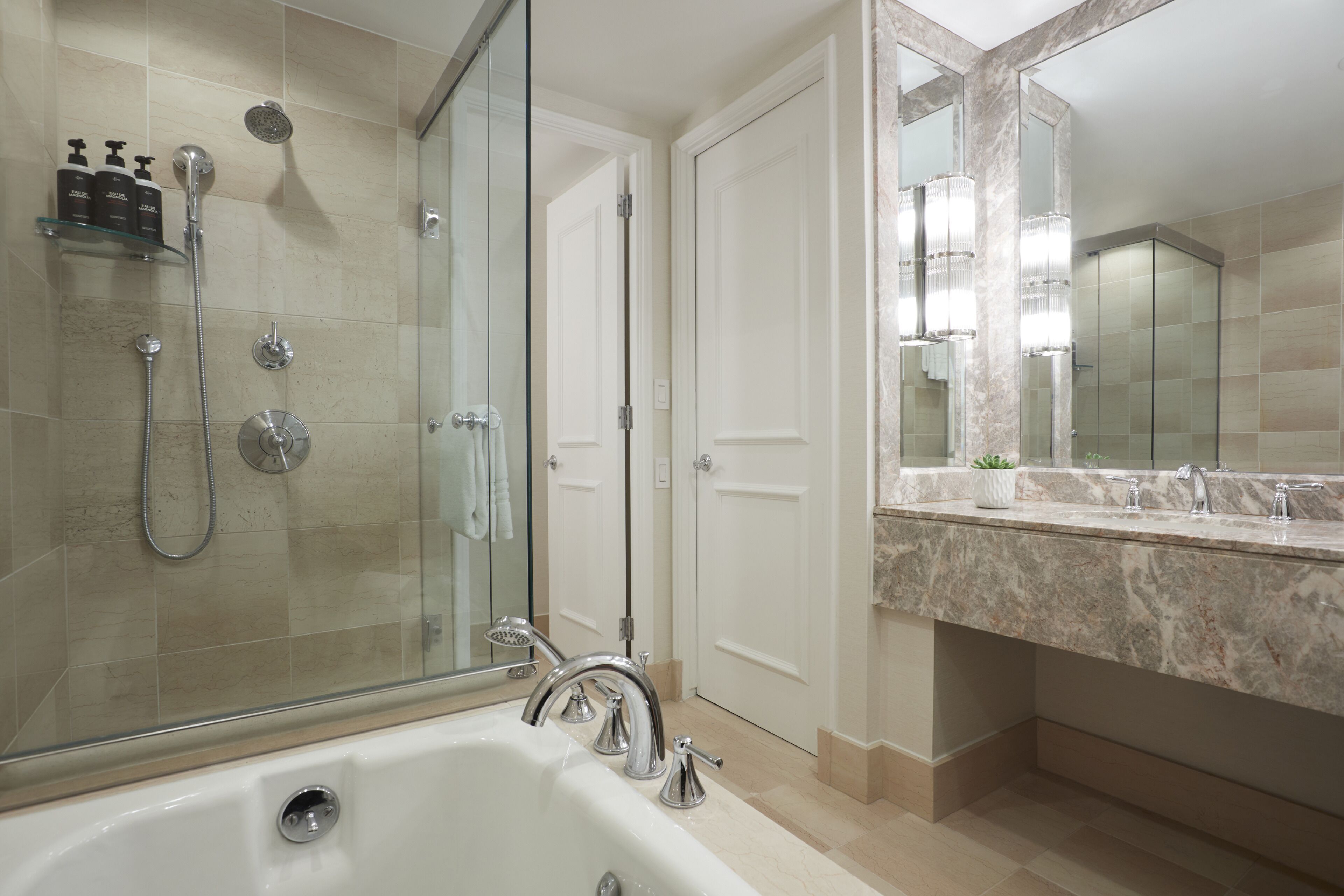 A modern bathroom with a glass-enclosed shower, a large bathtub, and a marble countertop with a sink.