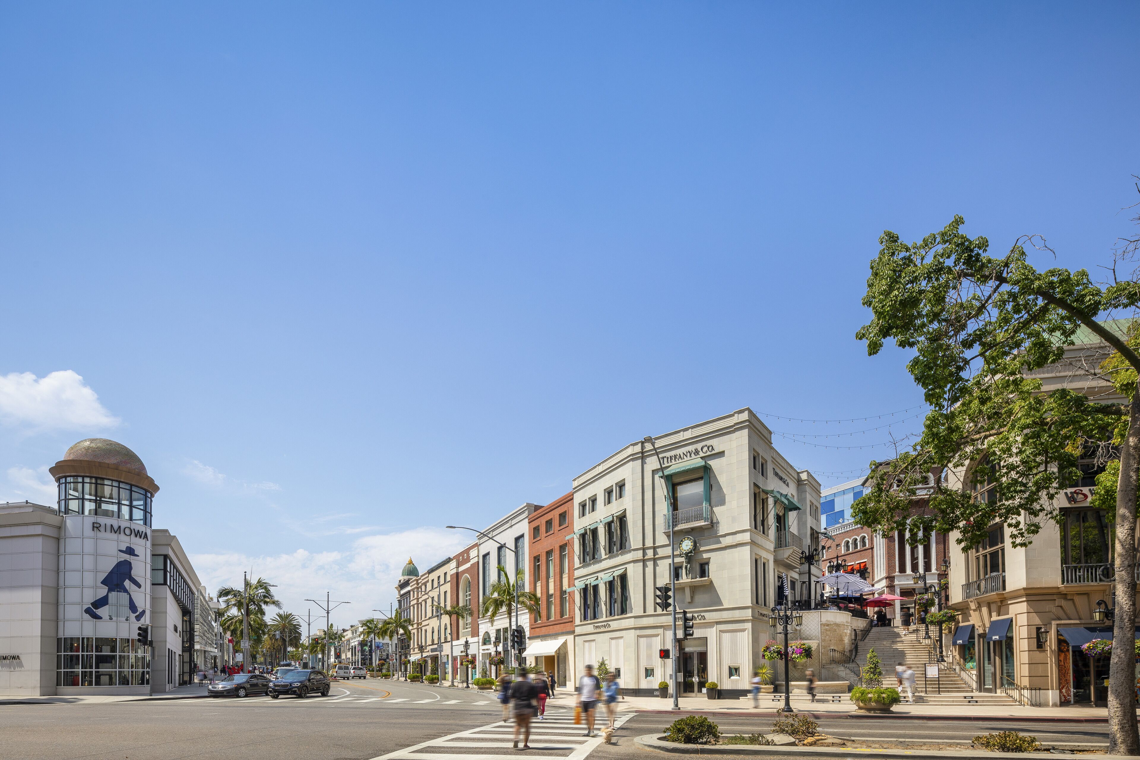 A street view with a Tiffany & Co. building, palm trees, and a pedestrian crossing.