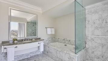 A modern bathroom with a marble sink, a large mirror, a glass-enclosed shower, and a view of the city.