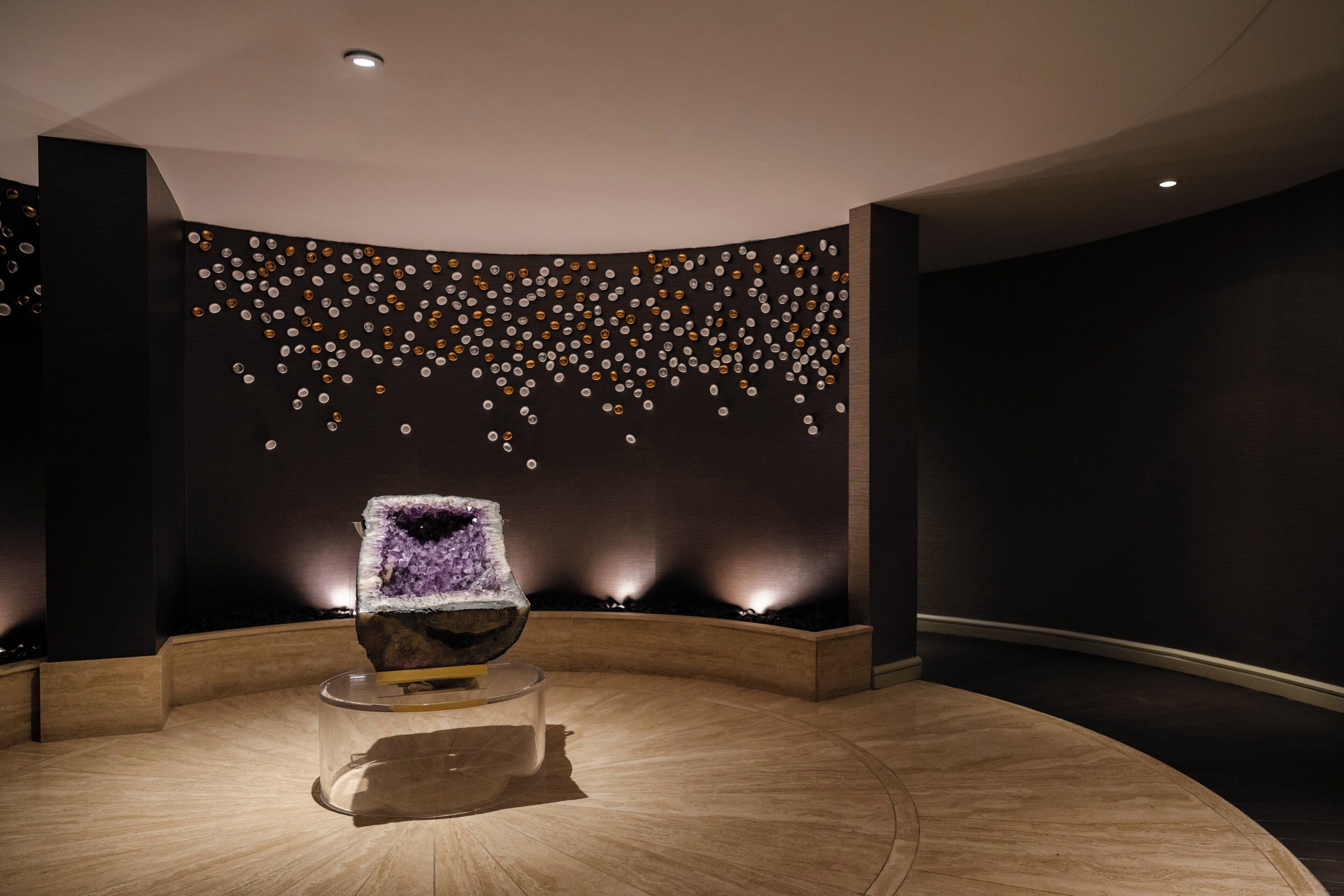 A modern interior with a central seating area featuring a clear glass table and a purple crystal centerpiece.