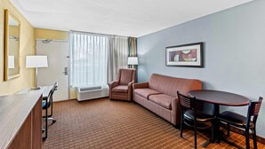 A hotel room with a desk, two chairs, a sofa, a dining table, and a large window with curtains. - Quality Inn Fort Dodge (Fort Dodge)
