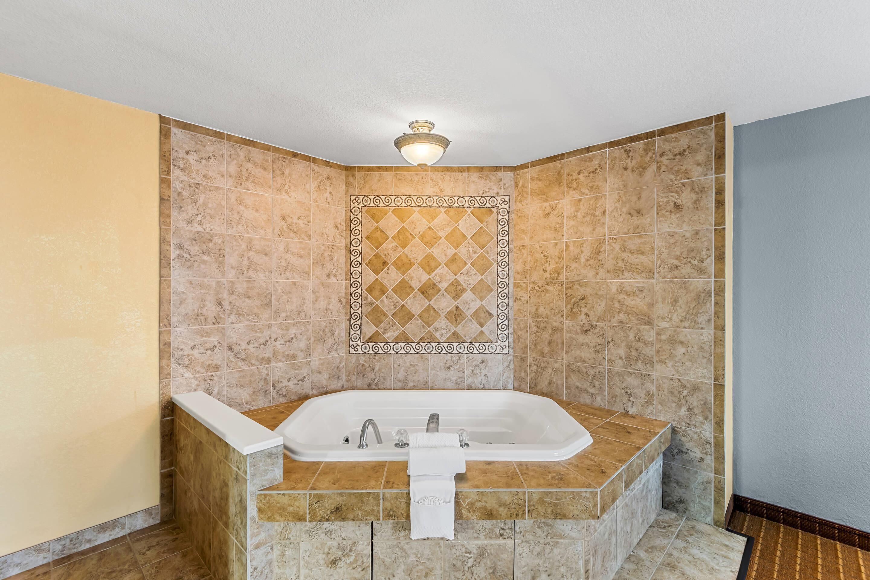 A corner bathroom with a freestanding bathtub, a decorative tile wall, and a ceiling light fixture.