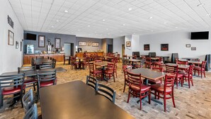 A spacious dining area with multiple tables and chairs, a kitchen in the background, and framed pictures on the walls. - Quality Inn Fort Dodge (Fort Dodge)