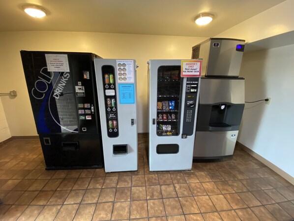 Three vending machines with drink and snack options, a water dispenser, and a sign indicating 'QUARTER'S ONLY' for certain items.