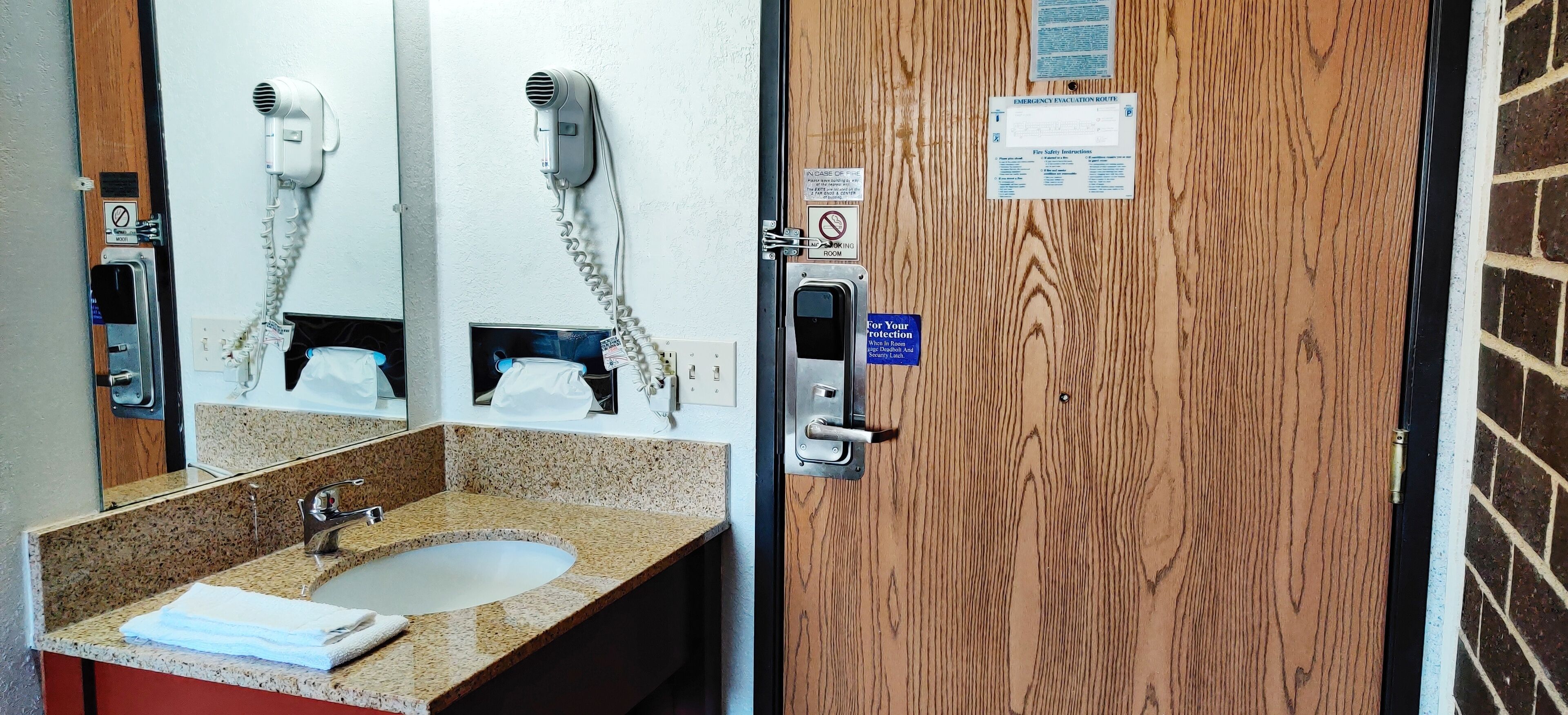Un baño con lavamanos de granito, un espejo, un secador de pelo y una puerta con instrucciones de emergencia.