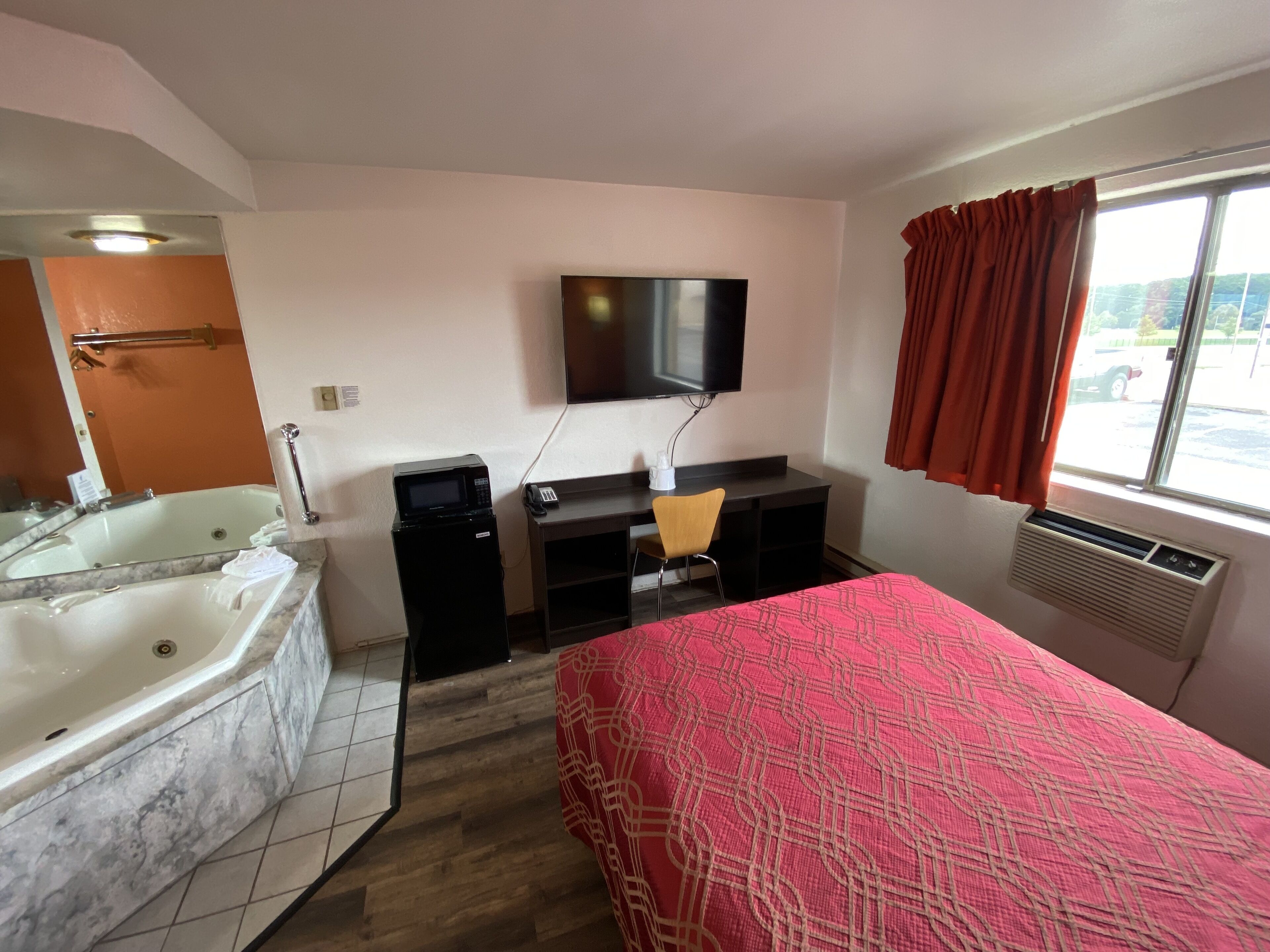 Une chambre d’hôtel avec un grand lit, un bureau avec une chaise, un téléviseur à écran plat, une baignoire et une fenêtre avec des rideaux.