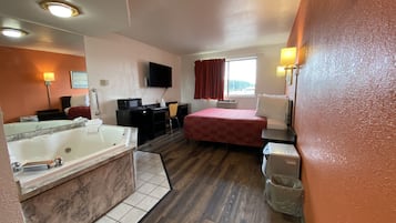 Une chambre d’hôtel dotée d’une grande baignoire, d’un bureau avec une chaise, d’un lit et d’un téléviseur fixé au mur.