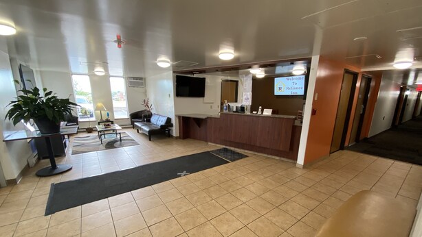 A hotel lobby with a reception desk, seating area, and a large potted plant. - Reliance Inn (Wausau)