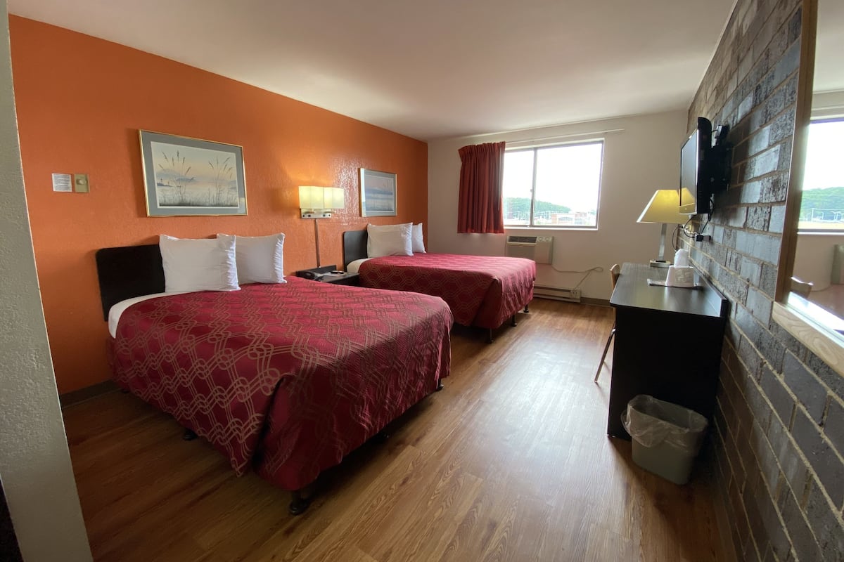 A hotel room with two beds, a desk, a TV, and a window with a view.
