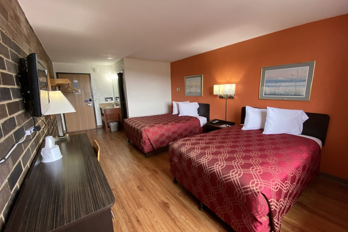 A hotel room with two beds, a desk, a TV, and a bathroom visible in the background.