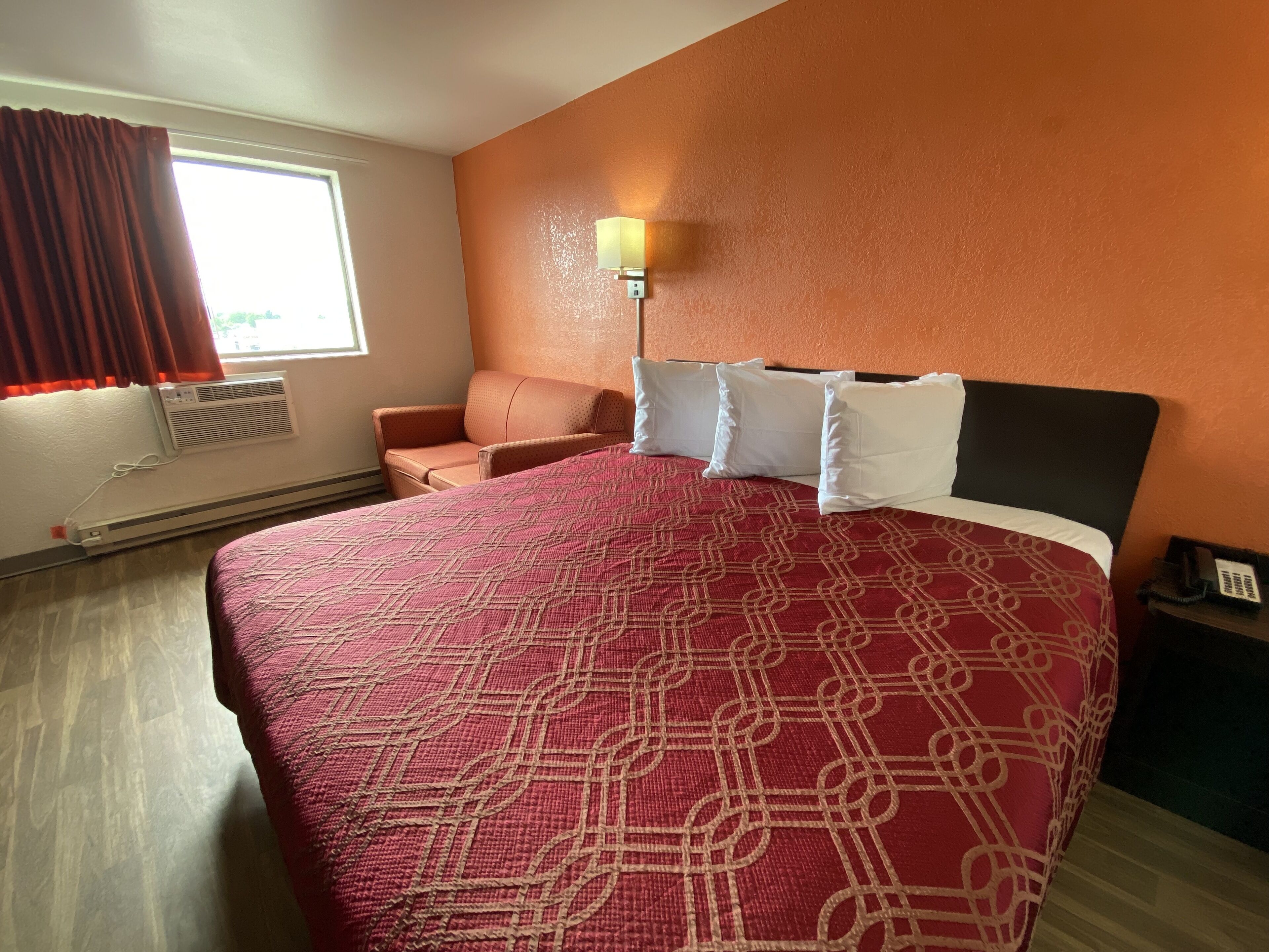 A hotel room with a large bed, a chair, a wall-mounted lamp, and a heater.