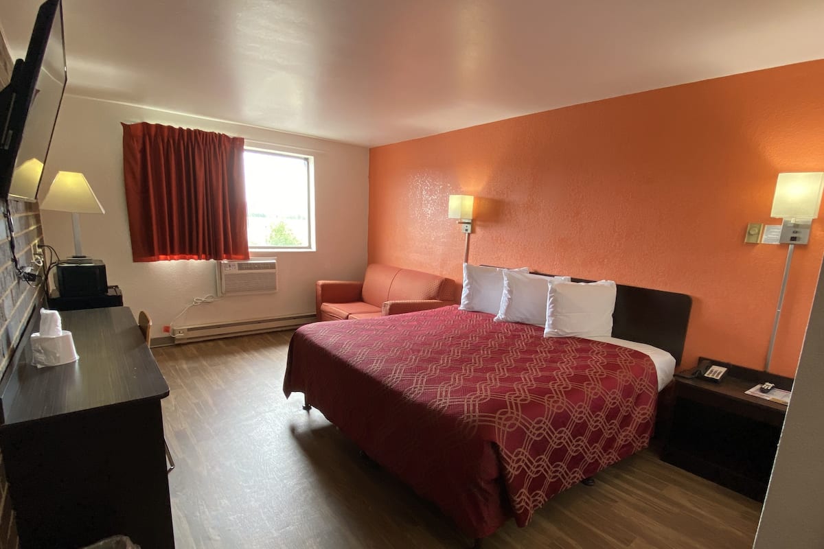 A hotel room with a bed, a desk, a chair, a lamp, and a window with curtains.