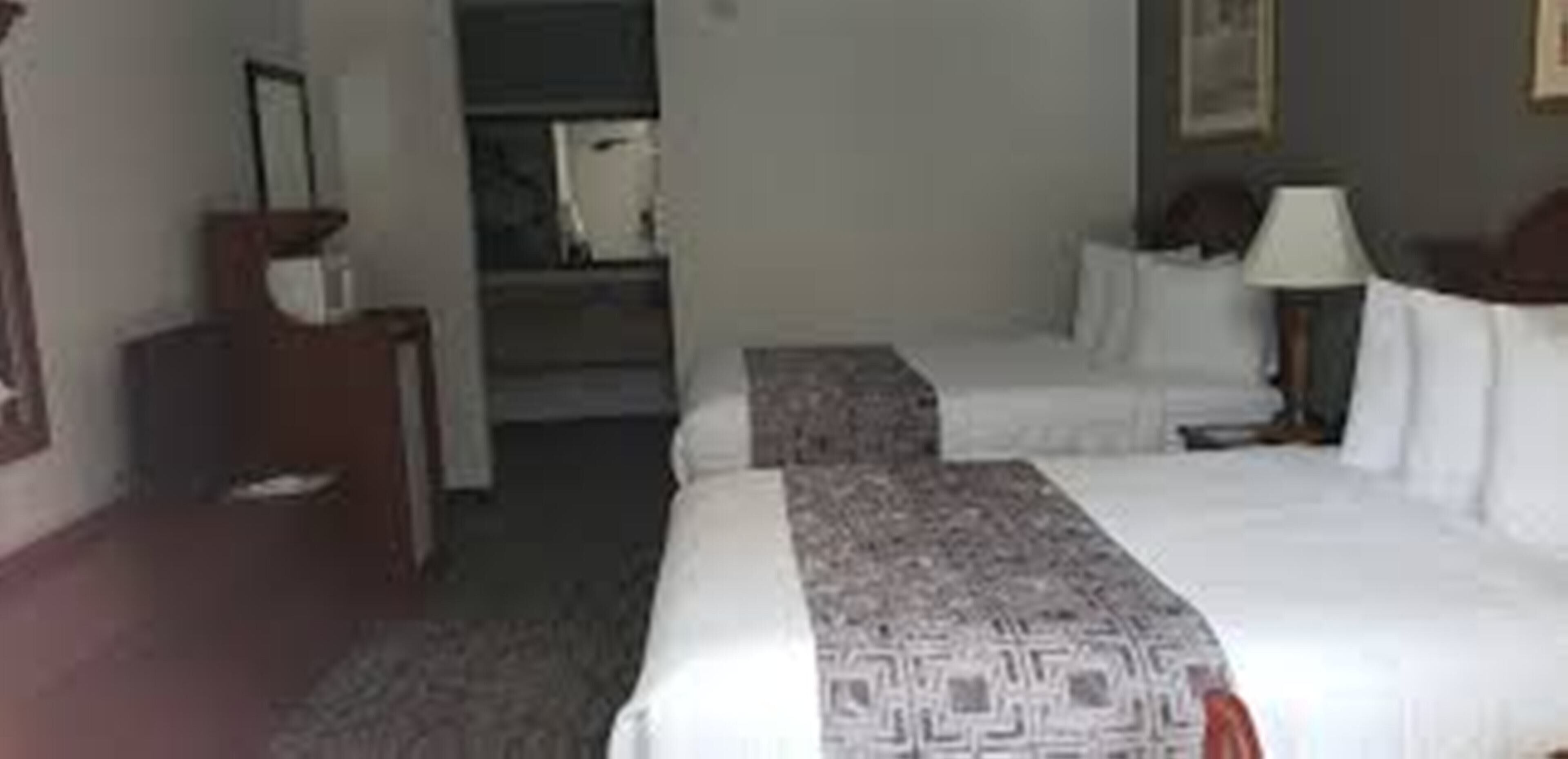 A hotel room with a bed, a nightstand, a lamp, and a dresser.