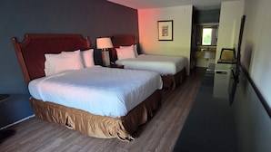 Quarto de hotel com duas camas, uma escrivaninha, uma cadeira, um espelho e uma janela.
