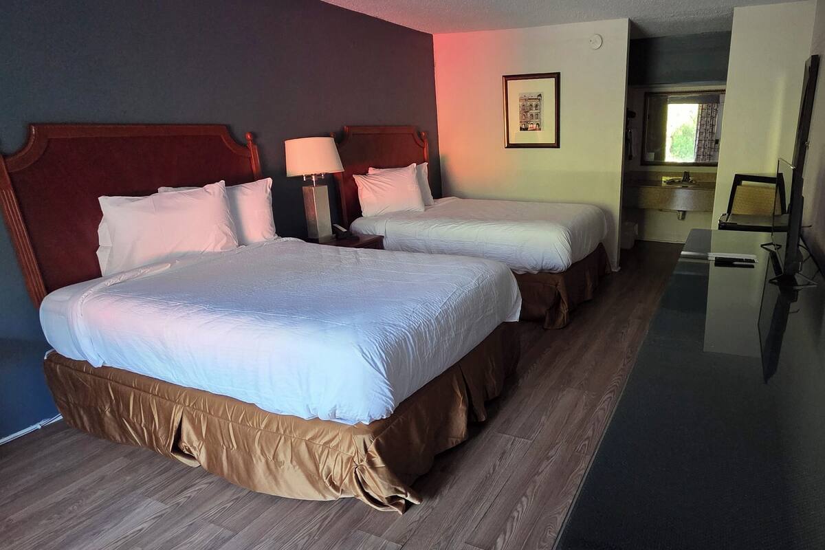Habitación de hotel con dos camas, un escritorio, una silla, un espejo y una ventana.