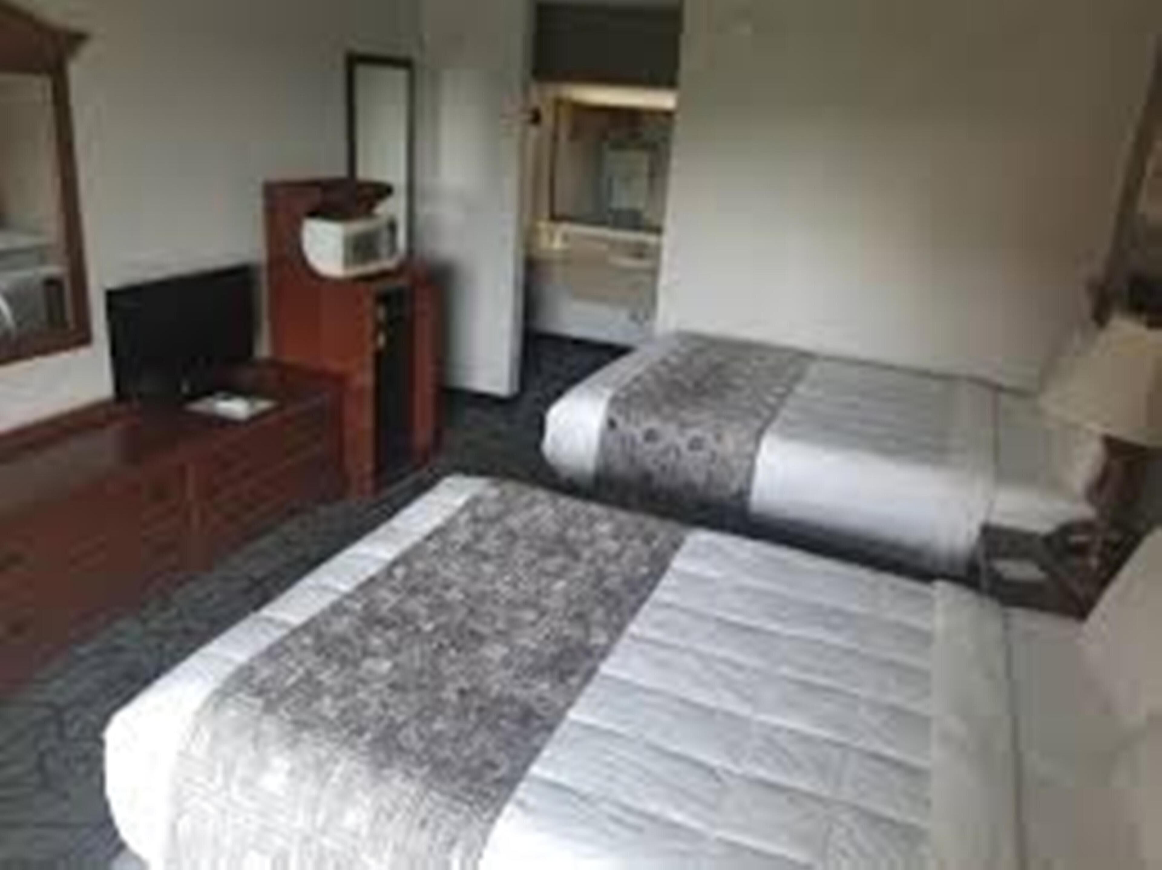 Une chambre d’hôtel avec deux lits, une commode, un téléviseur et un miroir.
