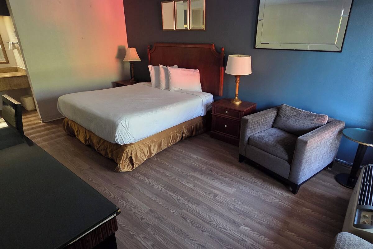 Una habitación de hotel con cama, mesitas de noche, escritorio, silla y ventana con cortinas.