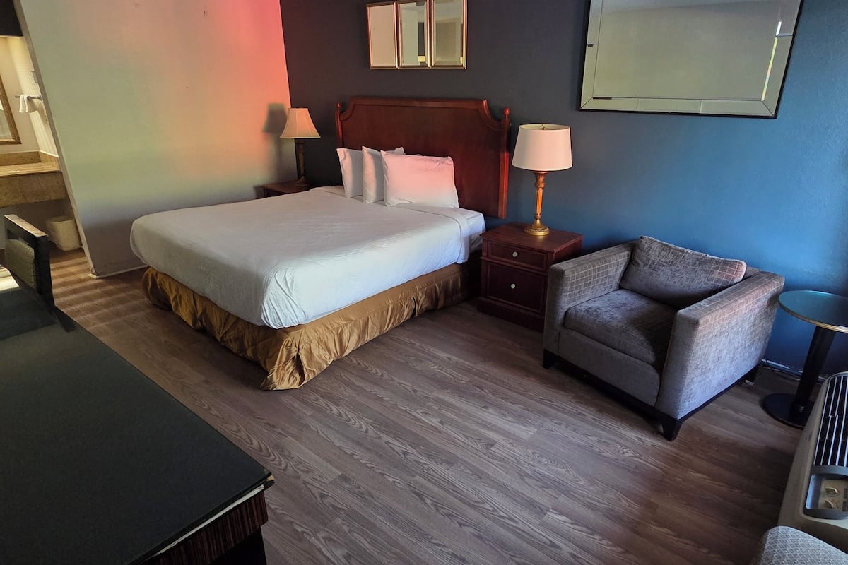 Una habitación de hotel con cama, mesitas de noche, escritorio, silla y ventana con cortinas.