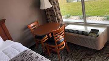 Une chambre d’hôtel avec un lit, une petite table, une chaise, une fenêtre donnant sur un espace verdoyant et un radiateur.