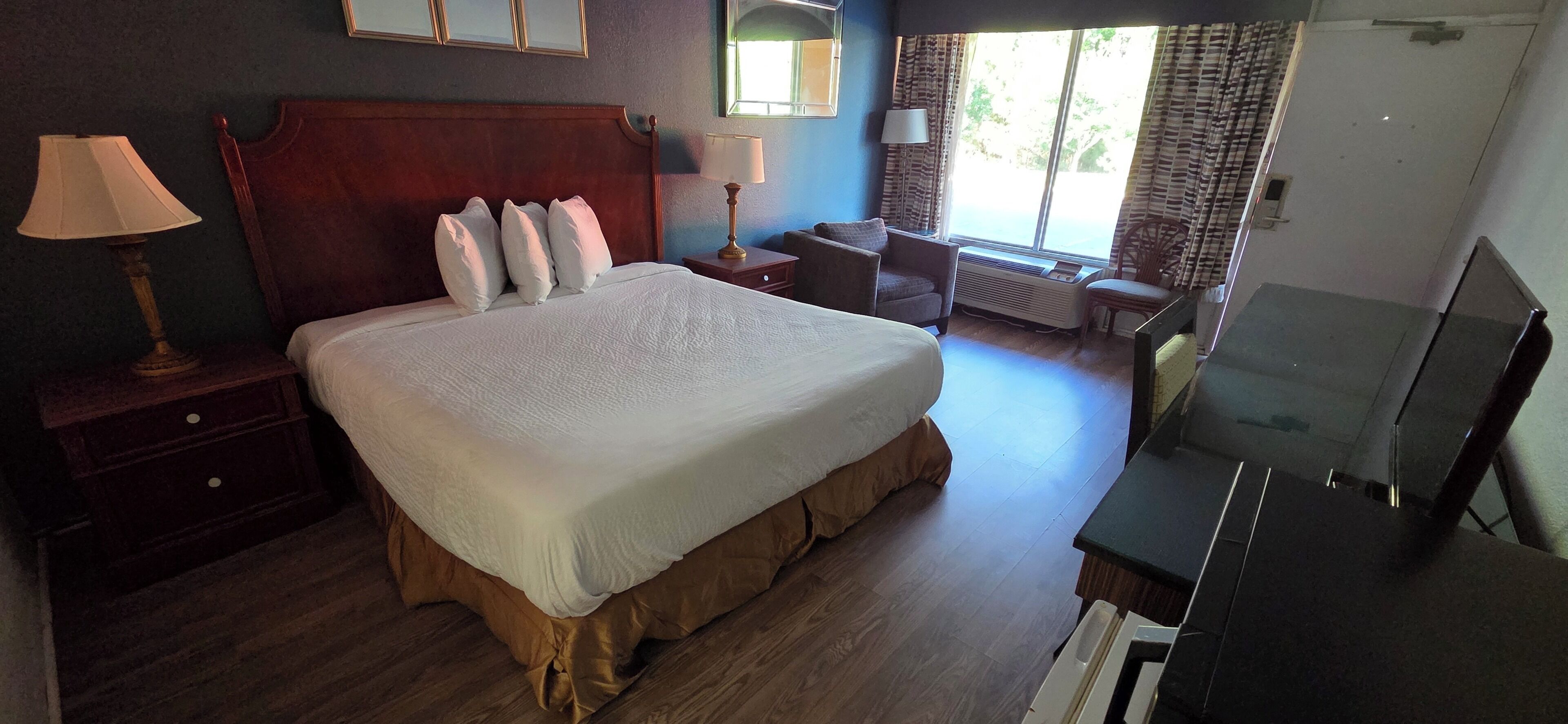 A hotel room with a large bed, bedside tables, a chair, a desk, and a television.