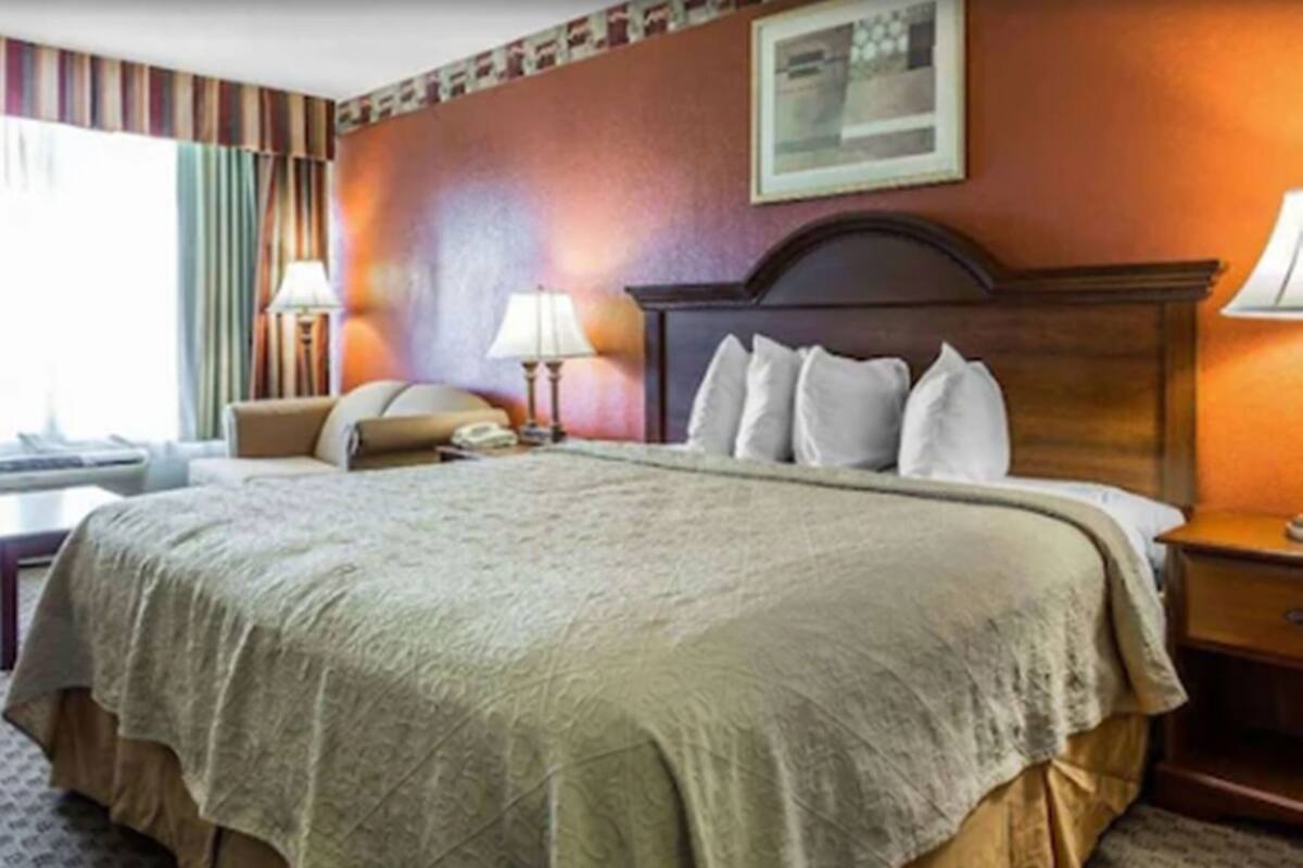 Habitación de hotel con una cama grande, un escritorio, una silla, una lámpara y un cuadro en la pared.