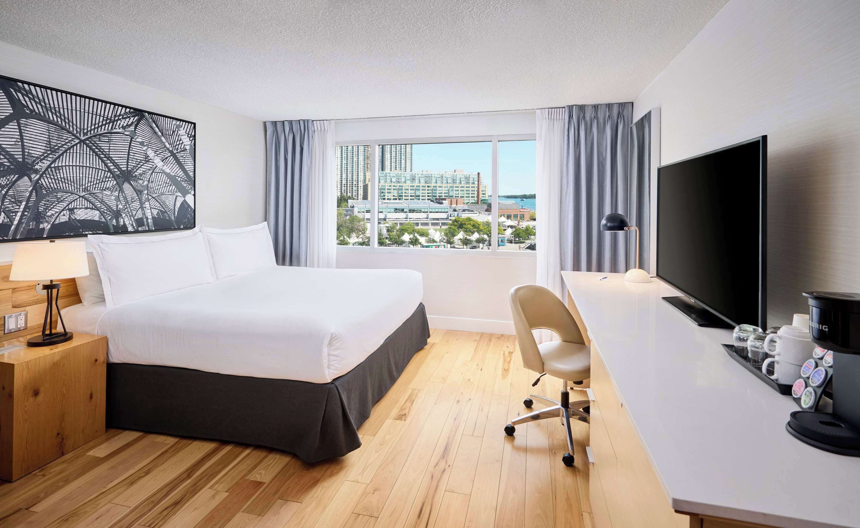 Ein Hotelzimmer mit Bett, Schreibtisch, Fernseher und Blick auf die Stadt.