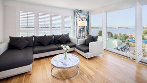 Een moderne woonkamer met een hoekbank, een ronde salontafel en uitzicht op water en gebouwen.