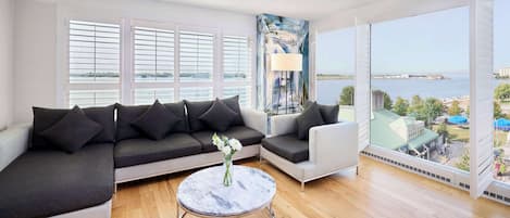 A modern living room with a sectional sofa, a round coffee table, and a view of the water and buildings.