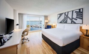 A hotel room with a large bed, a desk with a TV, a chair, and a view of a body of water through large windows. - Radisson Blu Toronto Downtown (Toronto)
