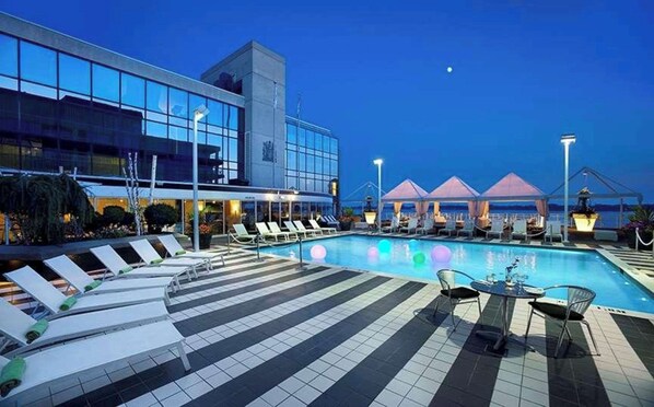 A modern hotel pool area with lounge chairs and umbrellas, a tiled deck, and a large building with reflective windows. - Radisson Blu Toronto Downtown (Toronto)