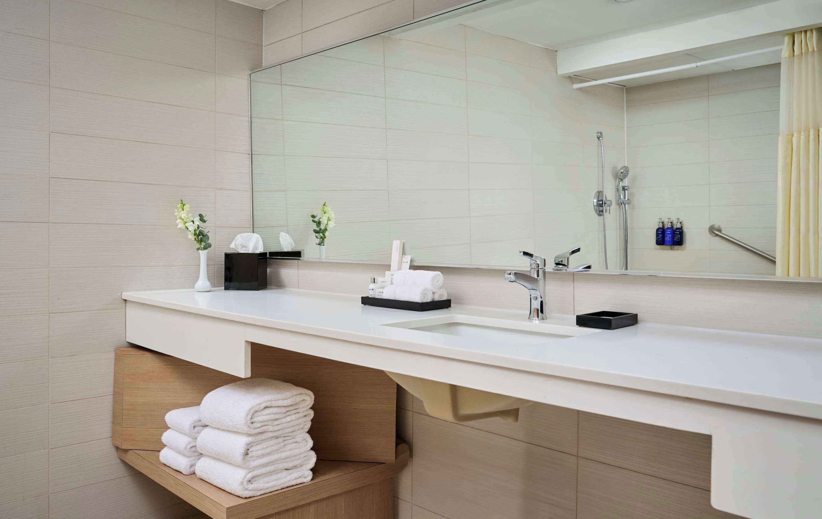 A modern bathroom with a large mirror, two sinks, a shower, and a towel rack.