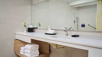 A modern bathroom with a large mirror, two sinks, a shower, and a towel rack.