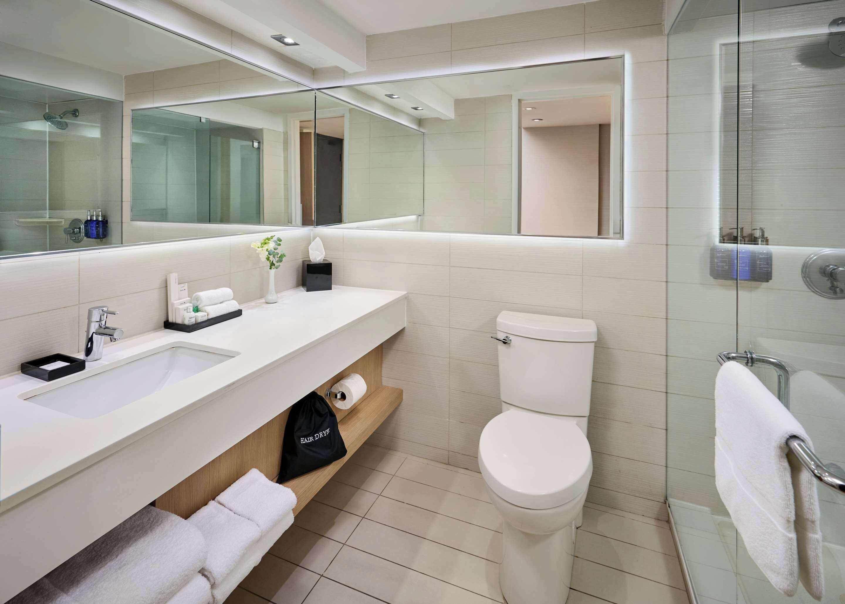 A modern bathroom with a large mirror, a sink, a toilet, and a glass shower enclosure.