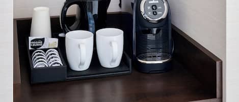 A kitchenette with a coffee maker, mugs, and a tea kettle on a wooden countertop.