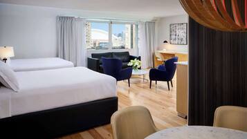 A hotel room with two beds, a desk, a sofa, and a view of the city.