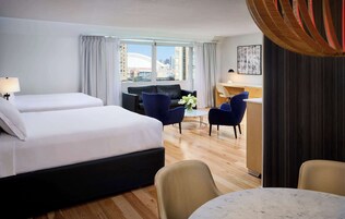 A hotel room with two beds, a desk, a sofa, and a view of the city.