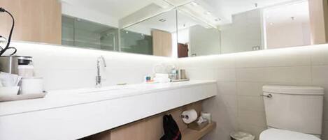 A modern bathroom with a white sink, mirror, and toilet. There is a trash can and a towel rack.