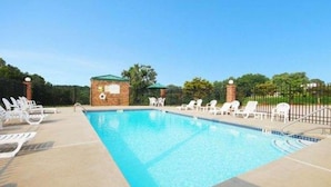 A rectangular swimming pool with clear blue water, surrounded by white lounge chairs and a brick structure with a green roof. - Quality Inn Dahlonega Near University (Dahlonega)