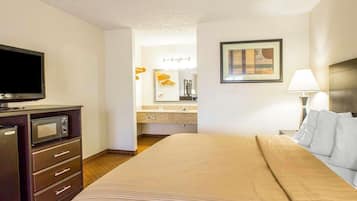 Une chambre d’hôtel équipée d’un lit, d’une télévision, d’un four à micro-ondes, d’une commode, d’une salle de bain avec un lavabo et un miroir, et d’un tableau encadré au mur.