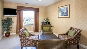 A room with a tiled floor, a television mounted on the wall, a large window with curtains, a framed picture on the wall, and two patterned chairs around a table. - Quality Inn Dahlonega Near University (Dahlonega)