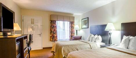 A hotel room with two beds, a TV, a desk with a lamp, and a window with curtains.