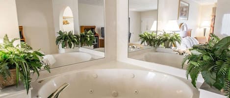 A modern bathroom with a freestanding bathtub, two large mirrors, and several potted plants.