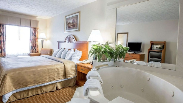 A hotel room with a large bed, a sitting area, a bathtub, a television, and a mirror. - Quality Inn Dahlonega Near University (Dahlonega)