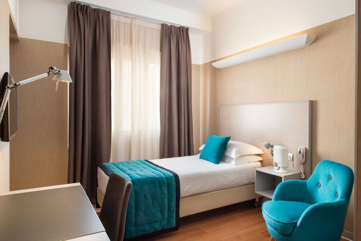A hotel room with a bed, a desk, a chair, a lamp, and a coffee maker.