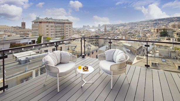 Una terraza en la azotea con dos sillas de mimbre blanco, una mesita redonda y una vista despejada del paisaje urbano.