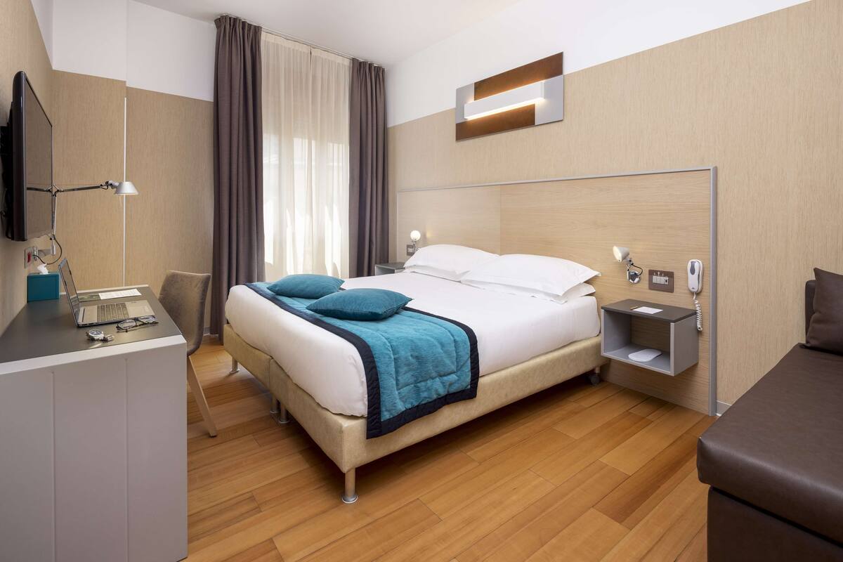 A modern hotel room with a bed, desk, and a flat-screen TV.