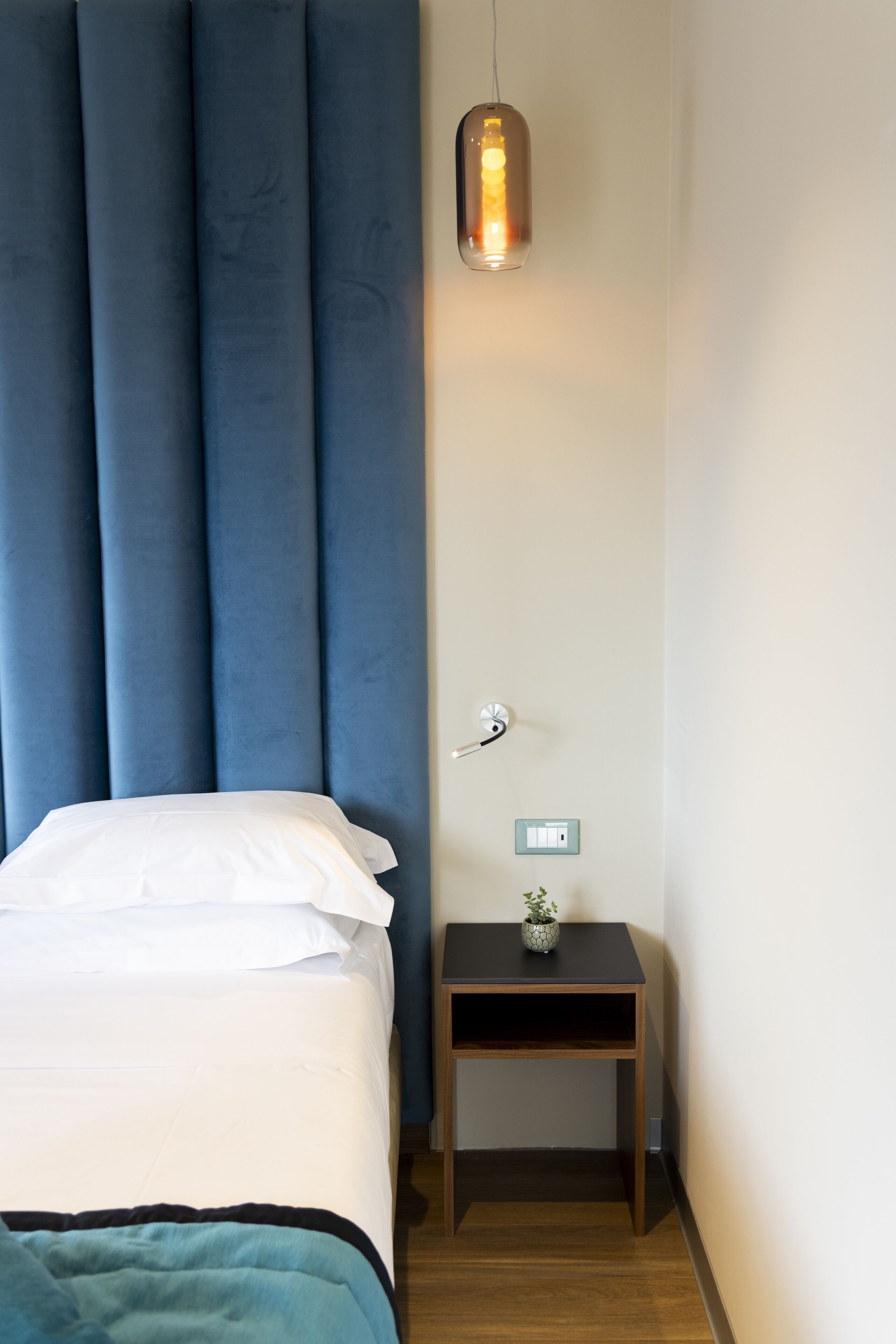 A bedroom with a bed, a bedside table with a plant, and a wall-mounted light fixture.