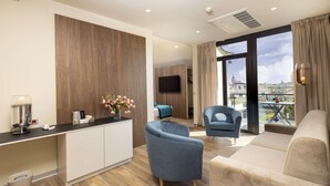 Habitación de hotel moderna con una pared de acento de madera, televisor de pantalla plana, sofá, sillón y vista a la ciudad.